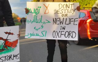 Placard reads: "DON'T DESTROY OUR NEW LIFE LIFE IN OXFORD".